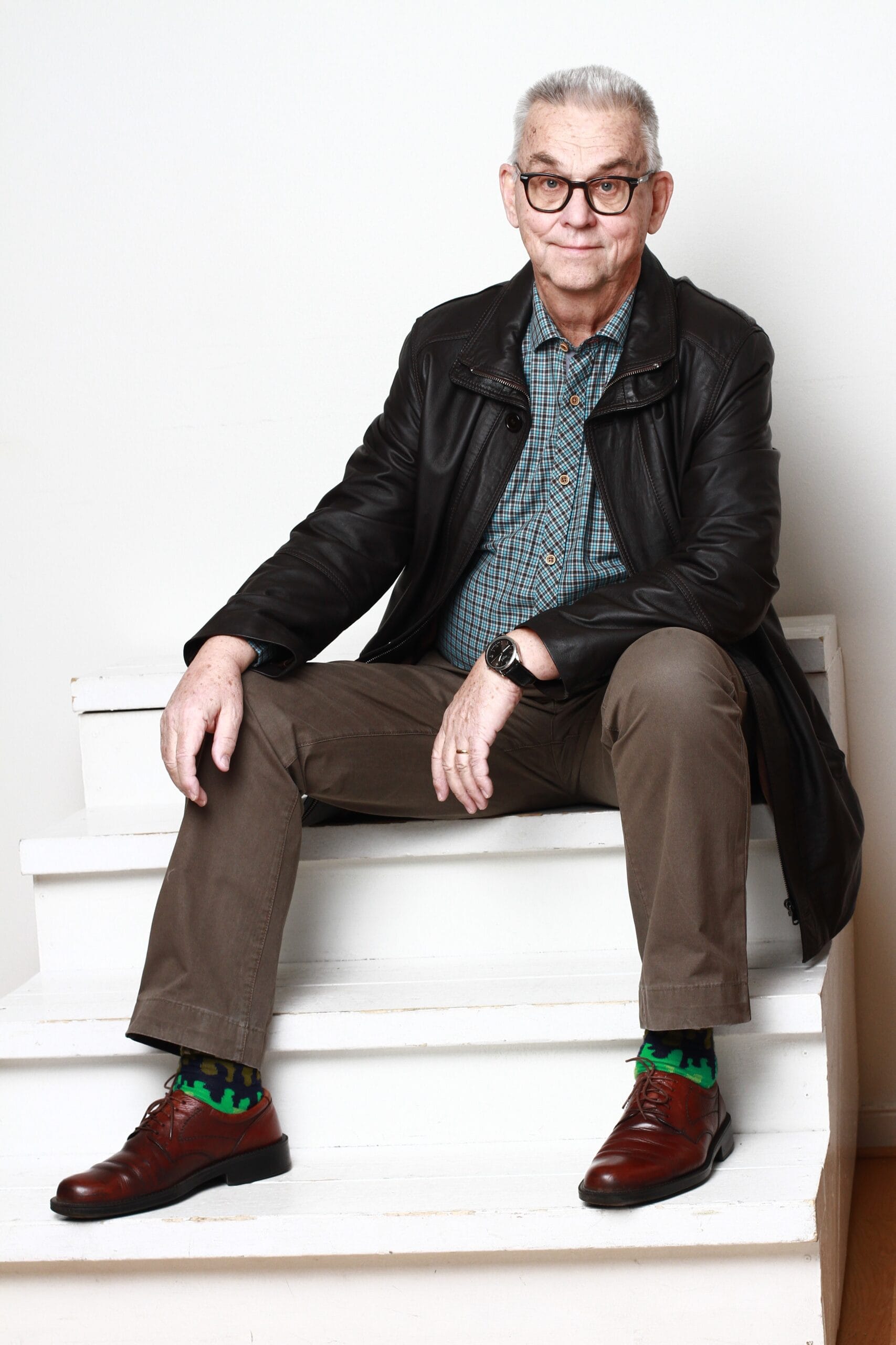 en man med glasögon, kavaj och kostymbyxor som sitter i en trappa