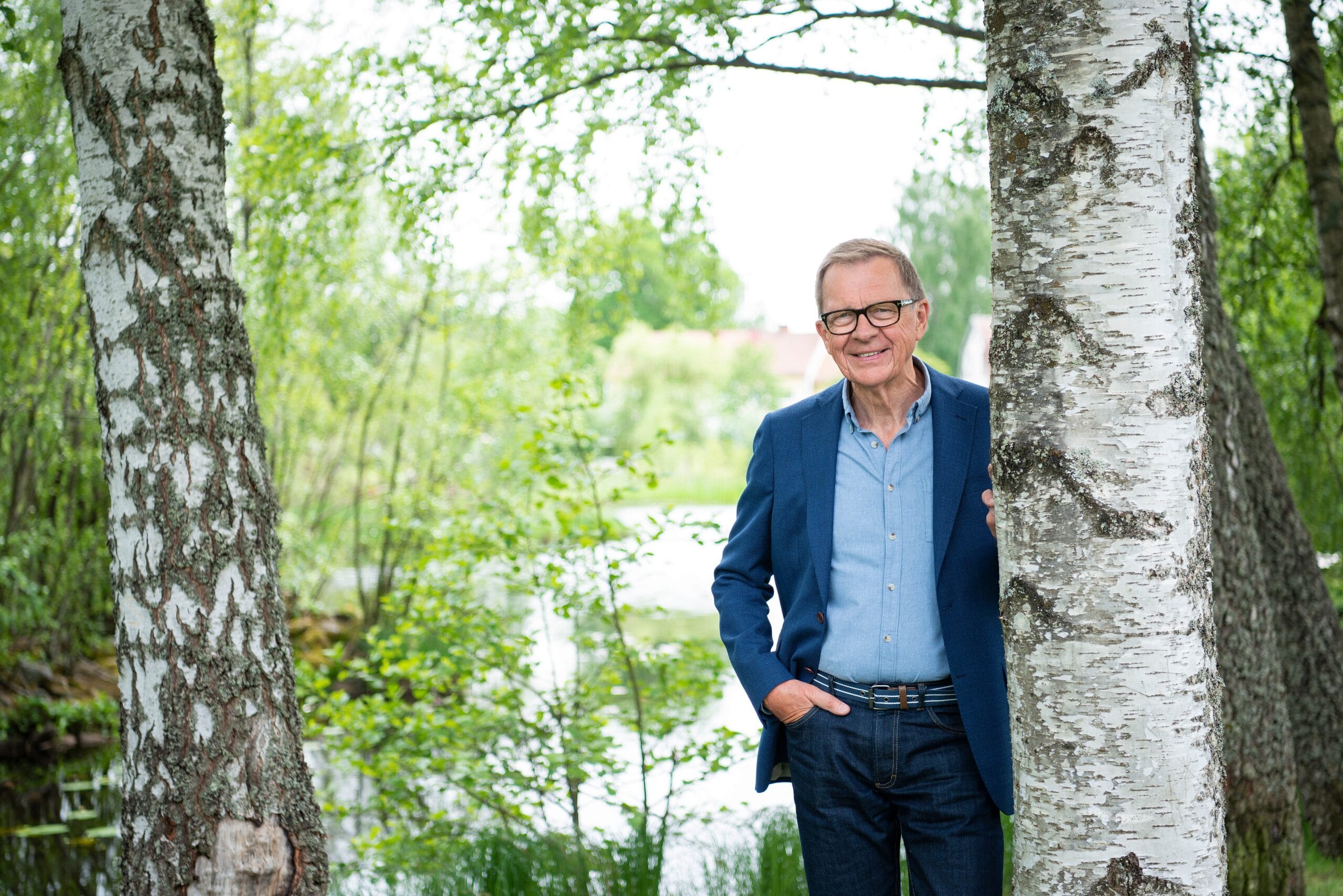 Man i kavaj och glasögon ståendes vid en björkstam.